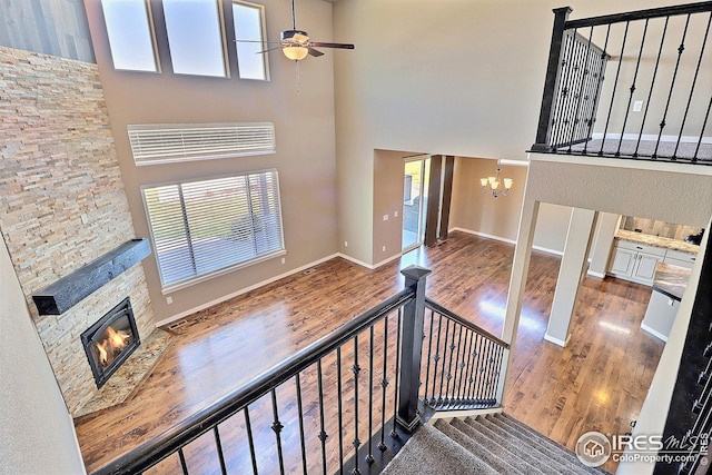 stairway featuring wood finished floors, plenty of natural light, ceiling fan with notable chandelier, a stone fireplace, and a high ceiling