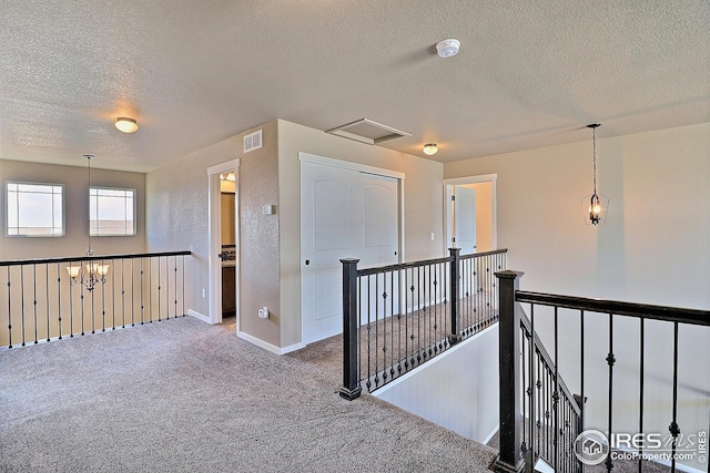corridor with a chandelier, carpet, an upstairs landing, visible vents, and a textured ceiling