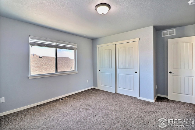 unfurnished bedroom featuring a closet, visible vents, dark carpet, and a textured ceiling
