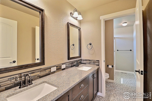 bathroom featuring double vanity, toilet, backsplash, and a sink