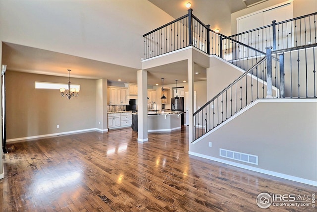 unfurnished living room featuring stairway, visible vents, a chandelier, baseboards, and dark wood-type flooring