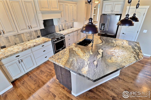 kitchen featuring premium appliances, wood finished floors, light stone countertops, and a sink