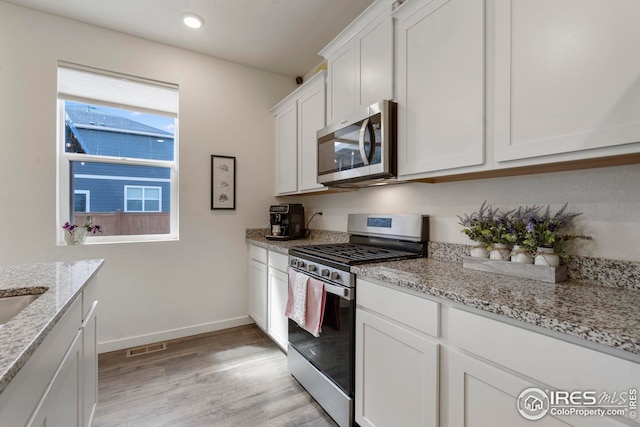kitchen with light stone counters, white cabinetry, stainless steel appliances, and light wood finished floors