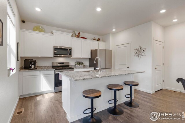kitchen with light wood-style flooring, visible vents, appliances with stainless steel finishes, and an island with sink