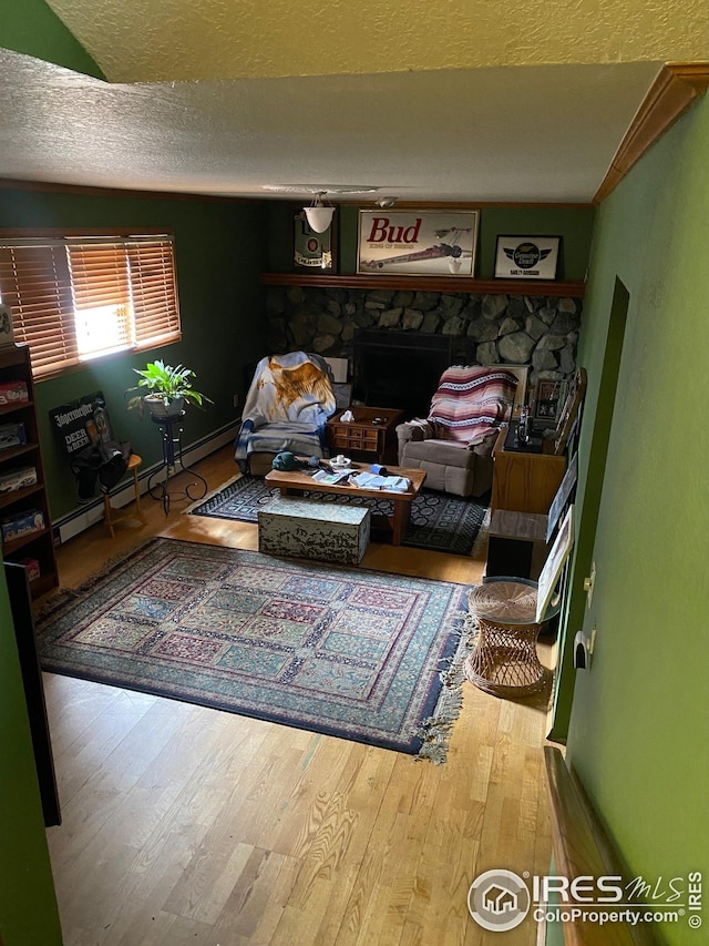 living area with a baseboard heating unit, a textured ceiling, wood finished floors, and a fireplace