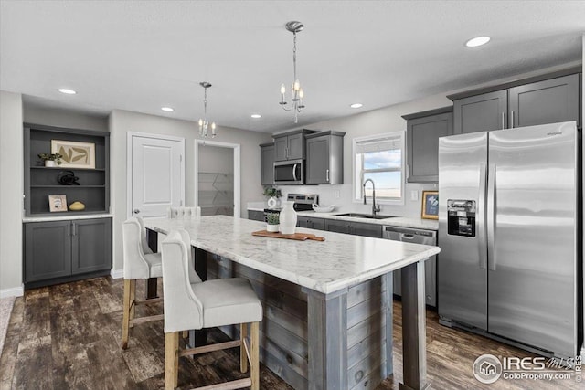 kitchen featuring dark wood-style floors, a sink, a notable chandelier, a kitchen island, and appliances with stainless steel finishes