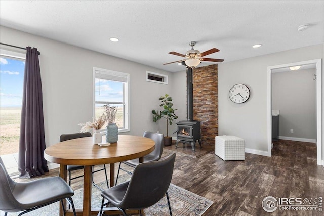 dining area with a wood stove, dark wood-style floors, baseboards, recessed lighting, and a ceiling fan