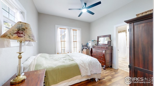 bedroom featuring ensuite bathroom, a ceiling fan, multiple windows, and light wood finished floors