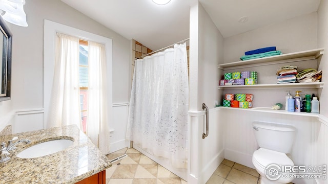 full bath featuring a shower with curtain, vanity, toilet, tile patterned flooring, and wainscoting