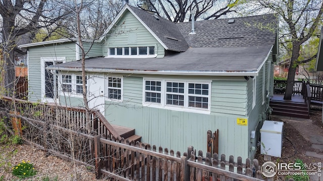 view of front of home with a deck, fence private yard, and a shingled roof