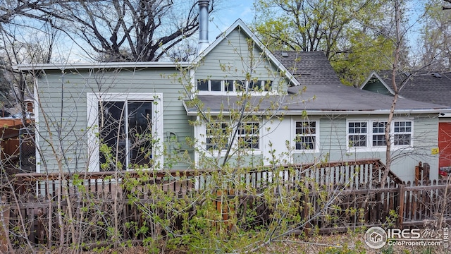 rear view of property featuring fence and a shingled roof