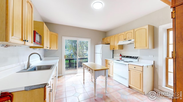 kitchen featuring light brown cabinetry, a sink, under cabinet range hood, and white appliances