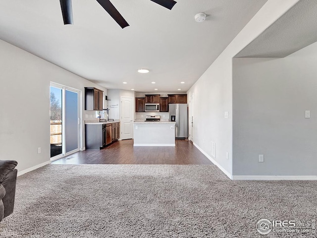 unfurnished living room featuring baseboards, dark carpet, a ceiling fan, and a sink