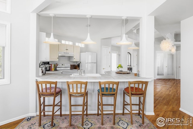 1891 Orchard Ave, Boulder, CO 80304 - kitchen with white appliances, a peninsula, wood finished floors, under cabinet range hood, and a kitchen breakfast bar