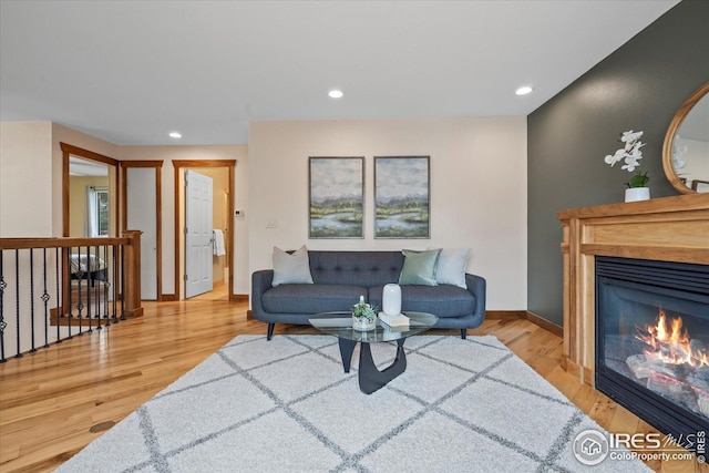 living area featuring baseboards, recessed lighting, light wood finished floors, and a glass covered fireplace