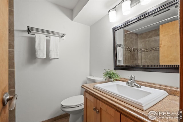 bathroom with toilet, a tile shower, and vanity