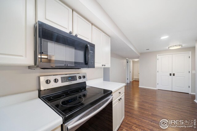 kitchen with electric stove, dark wood-style flooring, black microwave, white cabinetry, and light countertops