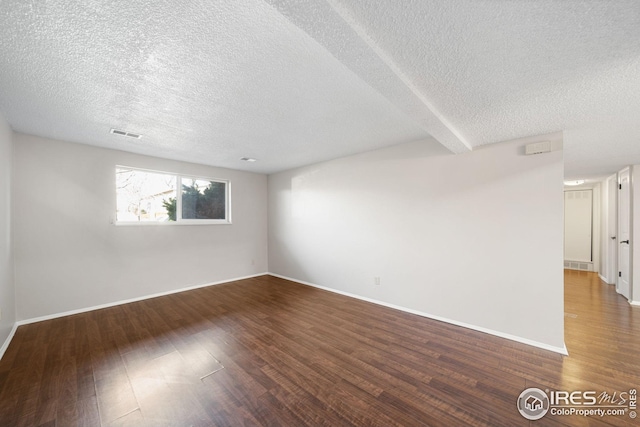 unfurnished room with a textured ceiling, visible vents, wood finished floors, and baseboards