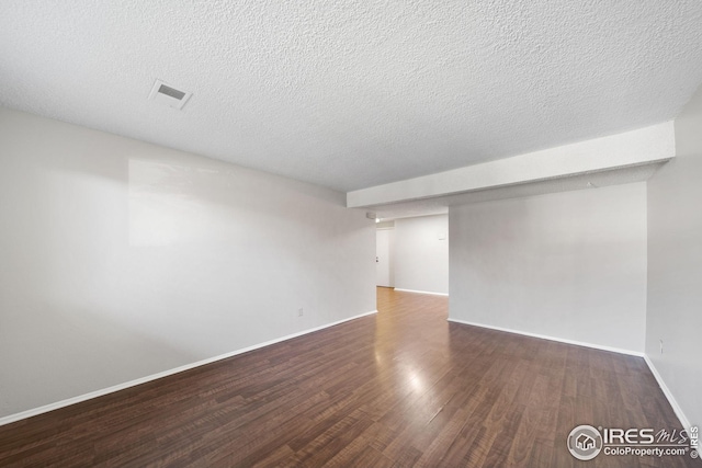 empty room featuring wood finished floors, visible vents, a textured ceiling, and baseboards