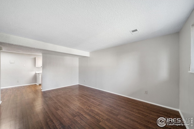 spare room with dark wood-style floors, a textured ceiling, and visible vents