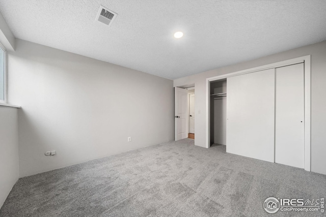 unfurnished bedroom featuring carpet, visible vents, a textured ceiling, and a closet