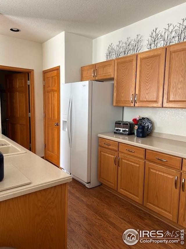 kitchen with white refrigerator with ice dispenser, brown cabinetry, light countertops, dark wood-style floors, and a textured ceiling
