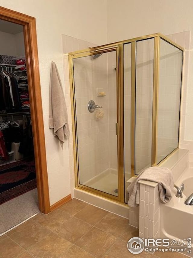 full bathroom featuring baseboards, a spacious closet, a shower stall, and a bath