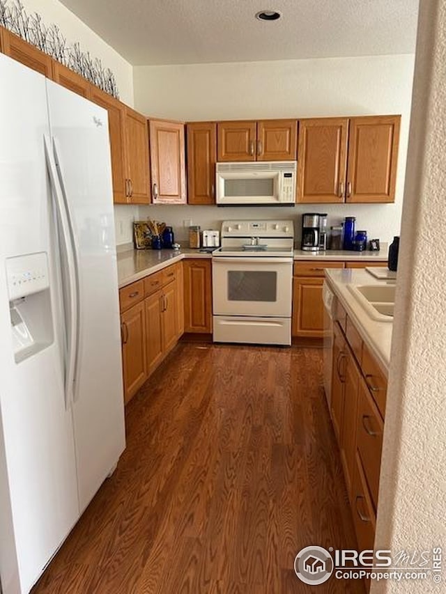 kitchen with a textured ceiling, a sink, light countertops, dark wood-type flooring, and white appliances