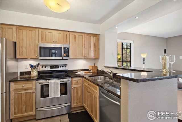 kitchen with a peninsula, light brown cabinets, dark stone counters, a sink, and appliances with stainless steel finishes