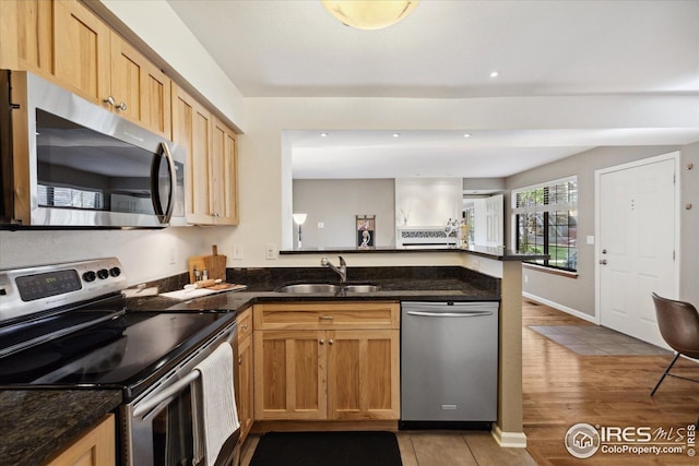 kitchen with appliances with stainless steel finishes, a sink, light tile patterned floors, a peninsula, and dark stone counters
