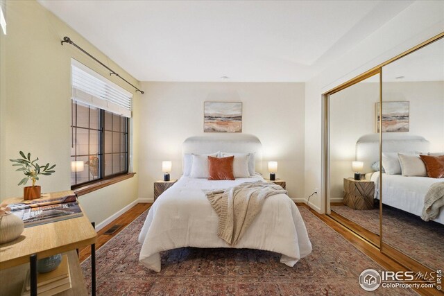 bedroom featuring baseboards, wood finished floors, visible vents, and a closet