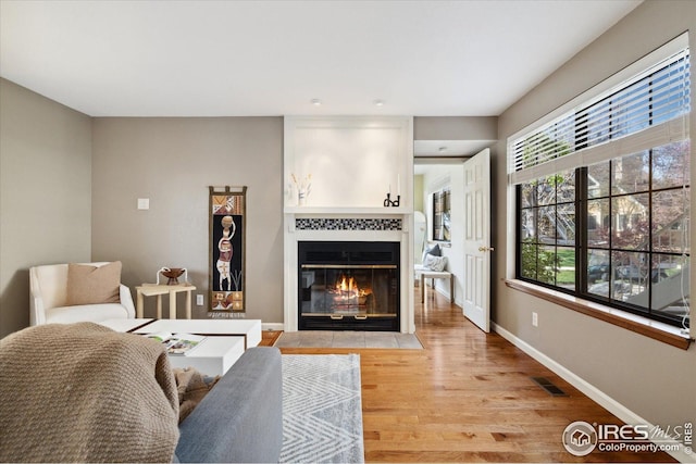 living room featuring baseboards, light wood finished floors, visible vents, and a tile fireplace