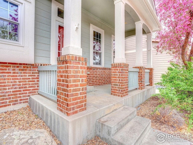 doorway to property featuring covered porch and brick siding
