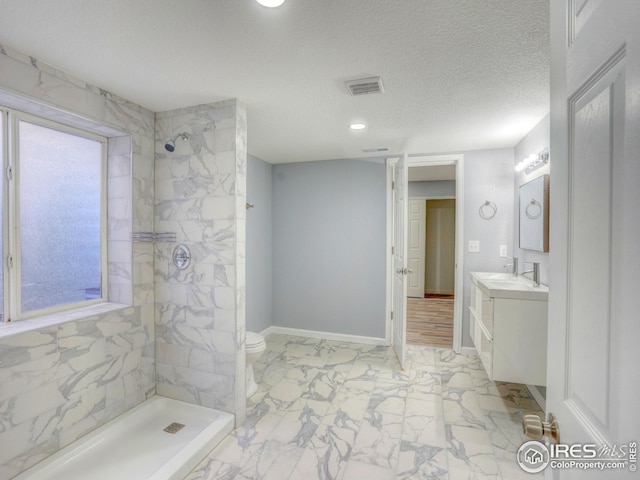 bathroom featuring marble finish floor, visible vents, tiled shower, and vanity