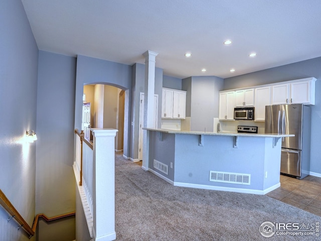 kitchen with a kitchen breakfast bar, baseboards, arched walkways, white cabinets, and appliances with stainless steel finishes