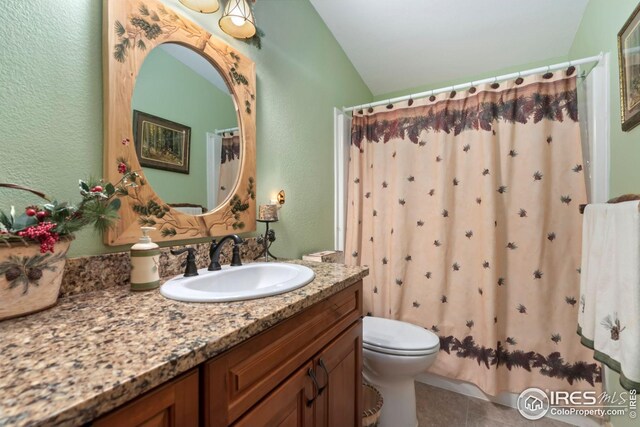 bathroom with lofted ceiling, a textured wall, toilet, tile patterned floors, and vanity