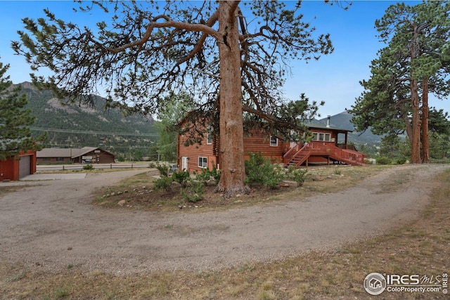 view of home's exterior featuring driveway, a garage, a deck with mountain view, and stairs