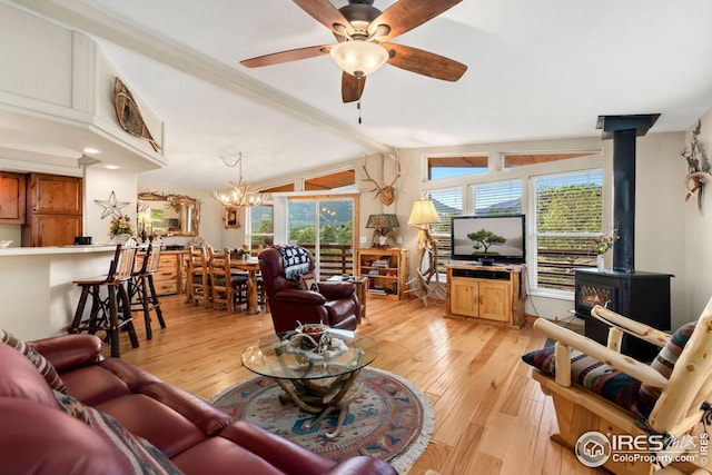 living area with a wood stove, ceiling fan with notable chandelier, vaulted ceiling, and light wood-style floors