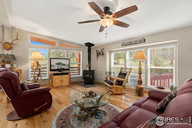 living room featuring a wood stove, a ceiling fan, light wood-style floors, and vaulted ceiling
