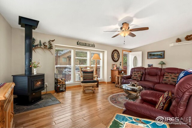 living room featuring wood-type flooring, a wood stove, a ceiling fan, and vaulted ceiling