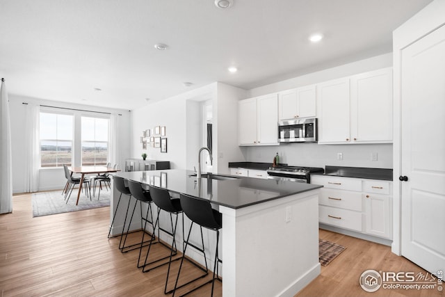 kitchen with dark countertops, a sink, stainless steel appliances, and a center island with sink