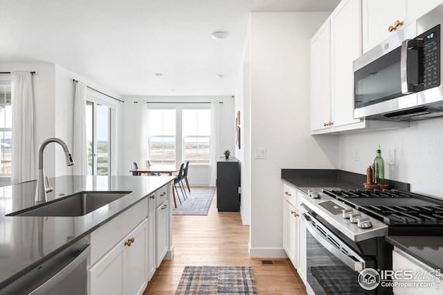 kitchen featuring light wood-style flooring, dark countertops, a sink, and appliances with stainless steel finishes