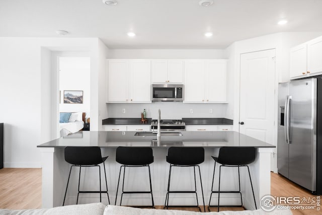 kitchen featuring white cabinets, a sink, appliances with stainless steel finishes, a breakfast bar, and light wood finished floors