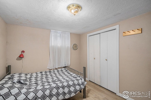 bedroom featuring a textured ceiling, baseboards, light wood finished floors, and a closet