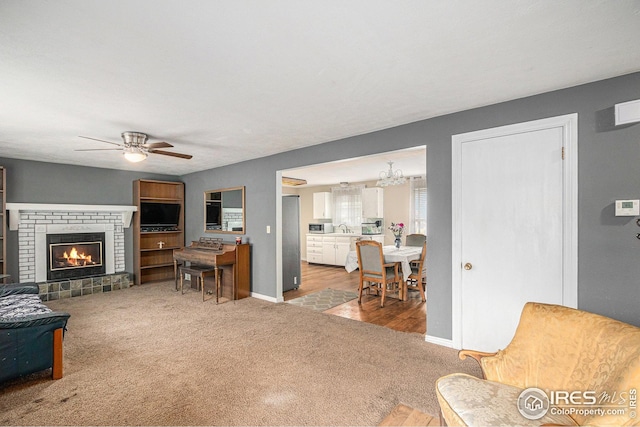 carpeted living area featuring a brick fireplace, a sink, a ceiling fan, and baseboards