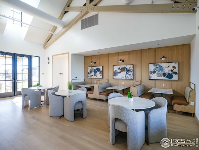 living area featuring beamed ceiling, light wood-style floors, visible vents, french doors, and high vaulted ceiling