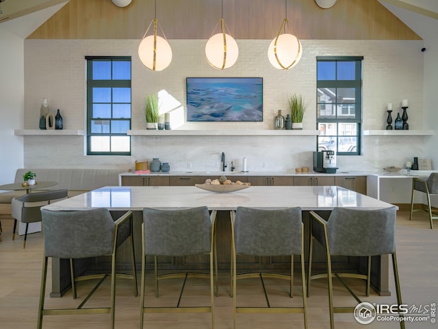 kitchen featuring a sink, a kitchen bar, light wood-type flooring, decorative light fixtures, and light stone counters