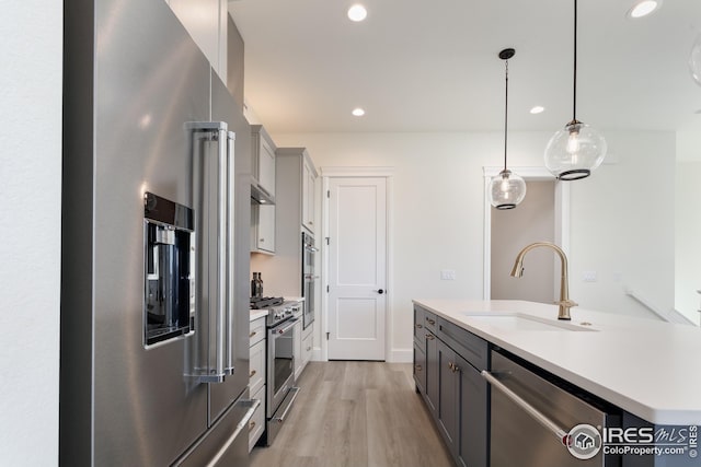 kitchen with light wood-style flooring, a sink, premium appliances, light countertops, and recessed lighting