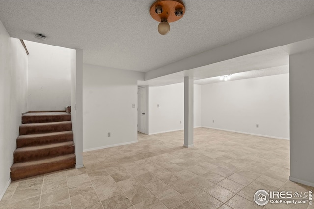 finished below grade area with stairway, baseboards, and a textured ceiling