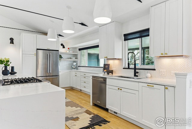 kitchen with decorative backsplash, open shelves, a sink, appliances with stainless steel finishes, and light wood-type flooring